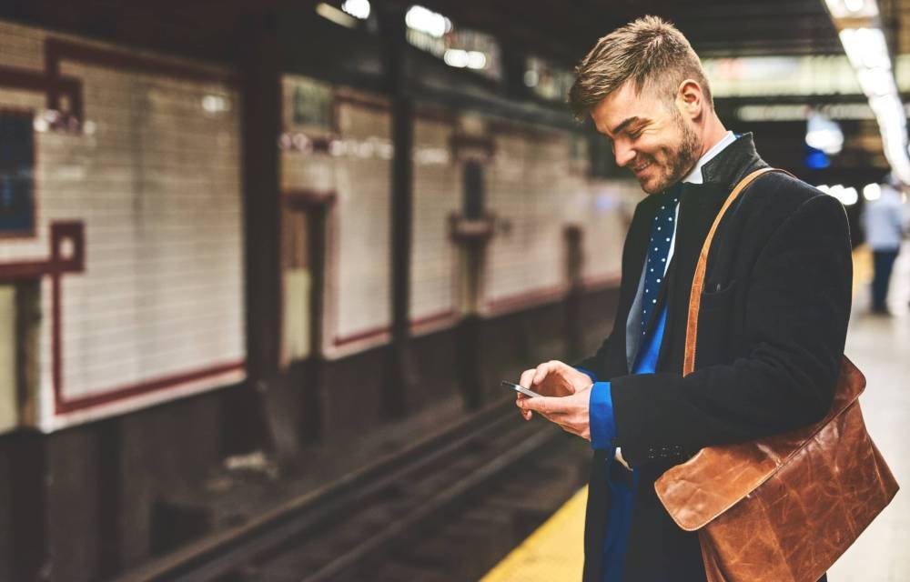 train-station-smile-business-man-with-smartphone-send-messages-communication-access-info-city-male-person-phone-with-mobile-app-social-media-multitasking-waiting (1)